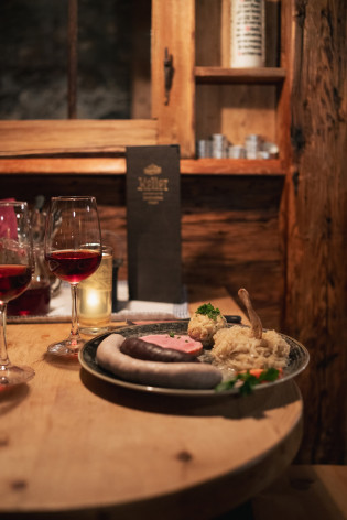 Tempo di Törggelen in Alto Adige Piatto con salsicce, carne, un canederlo e crauti accanto a calici di vino rosso in una stube rivestita in legno