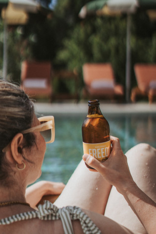 Relax a bordo piscina allo Schnitzbichlhof Donna con occhiali da sole e una bevanda a bordo piscina allo Schnitzbichlhof, con lettini e ombrelloni sullo sfondo