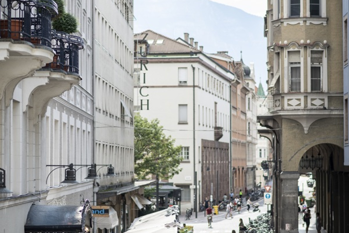 A spasso nel centro storico di Bolzano Via animata di Bolzano con tavolini all’aperto, ciclisti e facciate di edifici storici